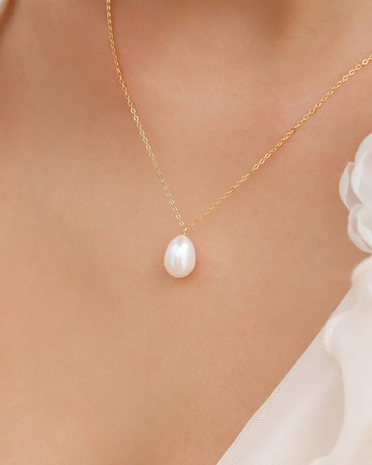 Gold necklace with a pearl pendant on a soft background