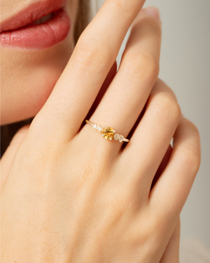 Close-up of a hand wearing a gold ring with a yellow gemstone on a neutral background