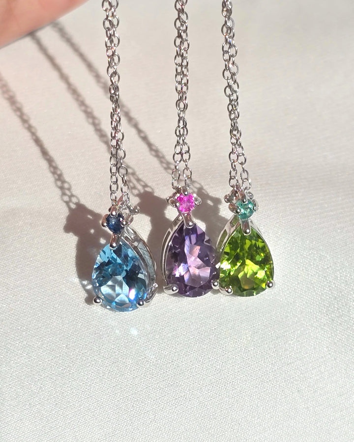 Three colorful teardrop pendants on a silver chain against a light background